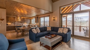 A spacious living area with a large sectional sofa, a dining table, and a kitchen in the background. - Birds Nest Retreat - Eagles Nest Village, hot tub, views, outdoor fireplace! (Banner Elk)
