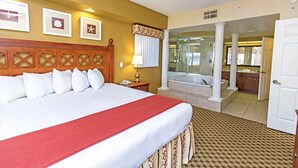 Quarto de hotel com uma cama grande, banheiro com banheira e vista para a cozinha.