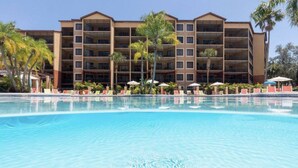 Um hotel com uma piscina grande, várias varandas e palmeiras.