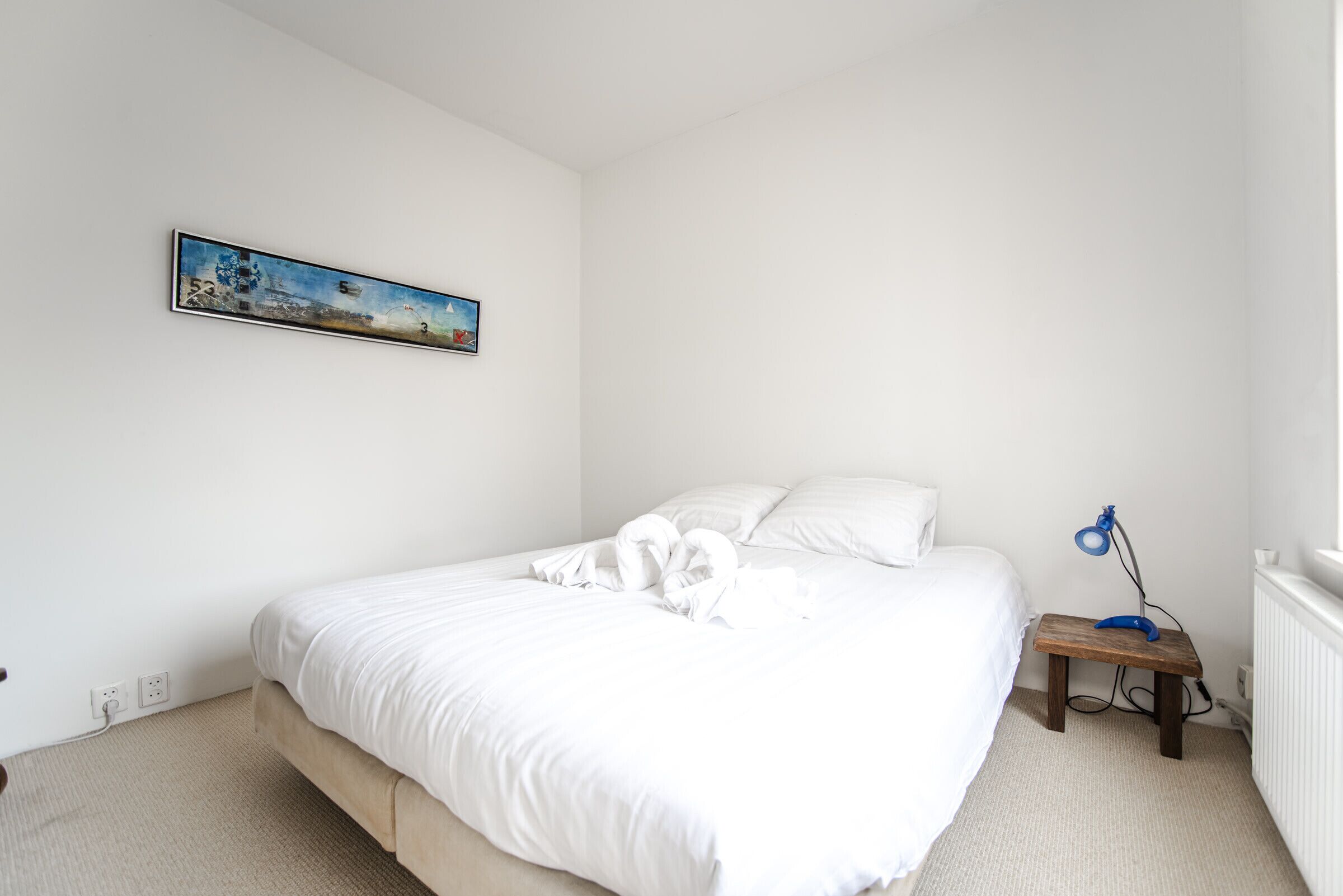 A neatly made bed with white linens and a blue lamp on a bedside table.