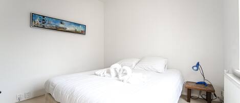 A neatly made bed with white linens and a blue lamp on a bedside table.