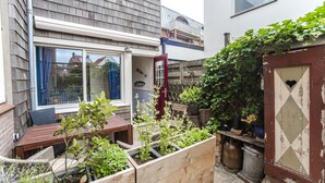 Een houten terras met een tafel en stoelen, omringd door verhoogde plantenbakken met diverse planten.