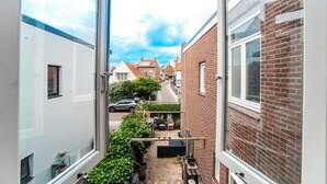 Een smalle steeg met een bakstenen gebouw aan de rechterkant en een wit gebouw aan de linkerkant. Achterin staat een auto geparkeerd op de straat.