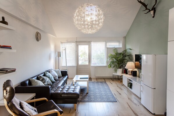 Uma sala de estar moderna com um sofá de couro preto, uma mesa de centro branca e uma luminária pendente.