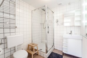 Ett modernt badrum med en dusch som är avskärmad med glasväggar, en toalett och ett handfat med spegel.