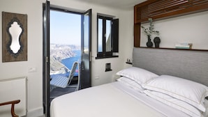 Un dormitori amb un llit, una cadira, una finestra que dona a una vista panoràmica i una estant amb objectes decoratius.