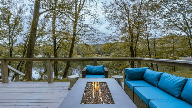 Une terrasse dotée d’un foyer, d’un espace salon et offrant une vue sur un lac entouré d’arbres.