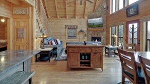 A wooden cabin interior with a dining area, a sofa, a fireplace, and a ceiling fan. - Welcome to Bearfeet Retreat, a pristine cabin in a quiet corner in the heart of Wears Valley. (Sevierville)