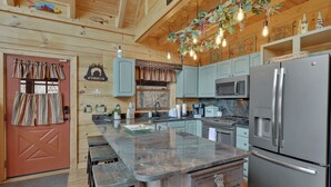 A kitchen with a large island, stainless steel appliances, and wooden cabinetry. - Welcome to Bearfeet Retreat, a pristine cabin in a quiet corner in the heart of Wears Valley. (Sevierville)
