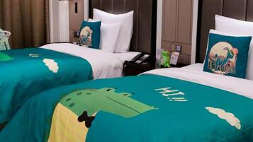 Two hotel beds with teal bedspreads featuring a cartoon frog design and the word 'HI!' on the bedspread.