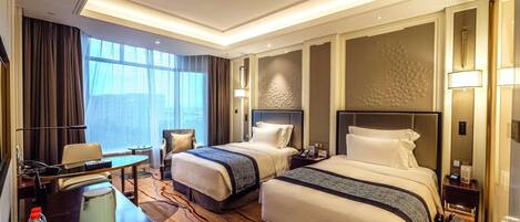 A hotel room with two beds, a desk, a chair, a coffee maker, and a view of the city.