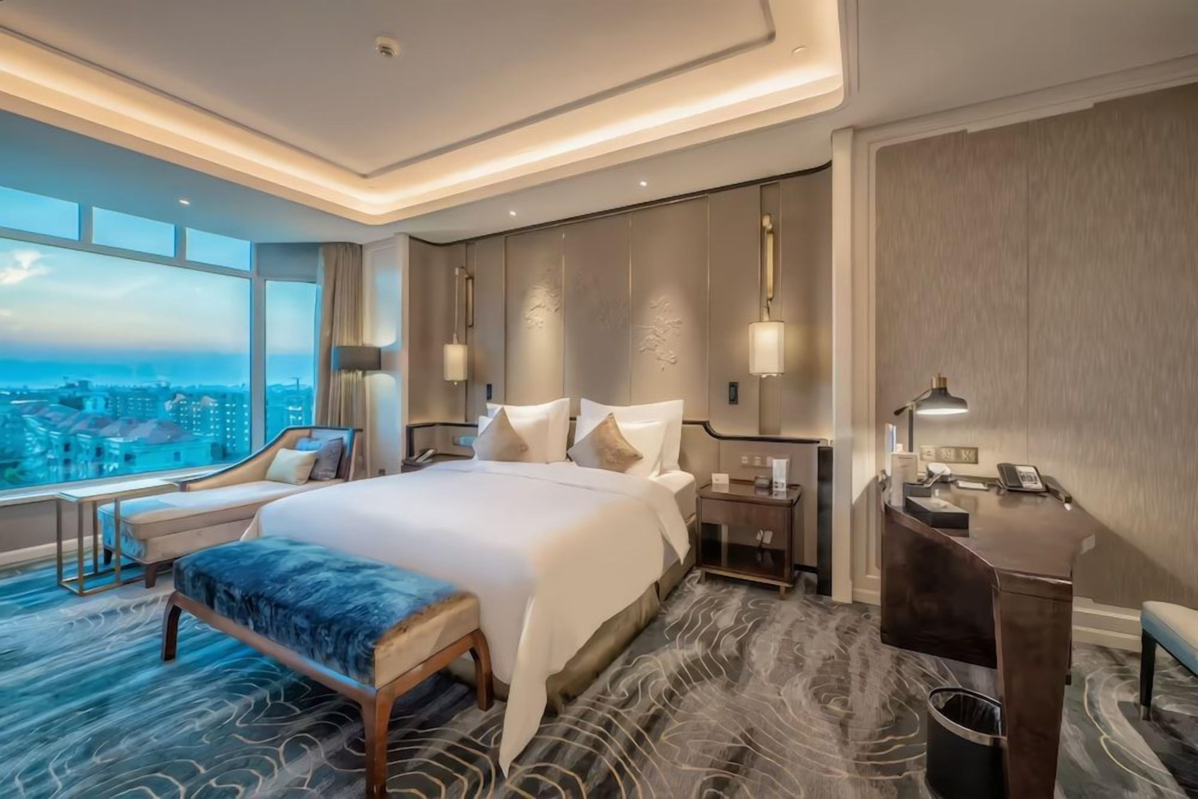 A hotel room with a large bed, bedside tables, a desk, and a view of the city.
