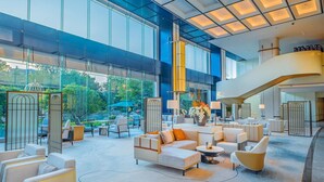 Een ruime lobby met een modern design, met een grote zithoek met banken en stoelen, een trap en grote ramen met uitzicht op de omgeving.