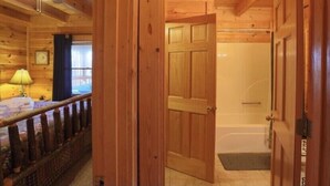 A wooden cabin interior with a bedroom, a bathroom with a bathtub, and a visible door. - Cabin w/ loft & beautiful updates, indoor fun/hot tub/new grill & communal pool! (Sevierville)