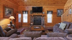 A log cabin interior with a stone fireplace, wooden walls, a television, and a cozy seating area. - Cabin w/ loft & beautiful updates, indoor fun/hot tub/new grill & communal pool! (Sevierville)