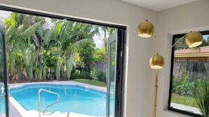 A modern room with a glass door leading to a pool, a round gold floor lamp, and a small table with a plant. - Gorgeous 3B/2B Private Heated Pool mins from the beach  (Pompano Beach)