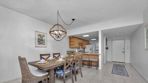 A dining area with a wooden table and chairs, a chandelier, and a kitchen in the background. - Gulf front! 3rd floor right on the beach! With free beach service (Navarre)