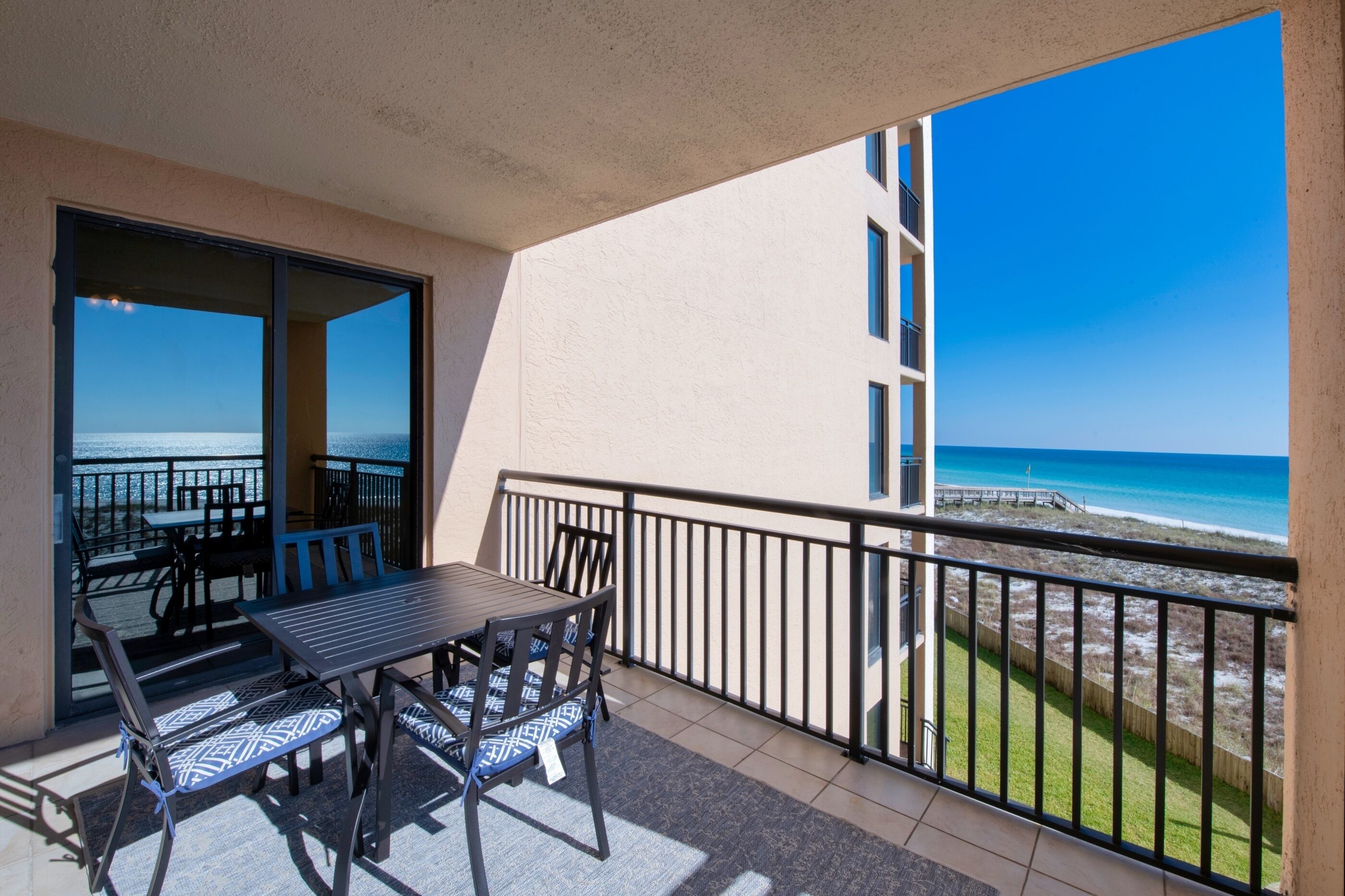 A balcony with a table and chairs, a view of the beach, and a building in the background.