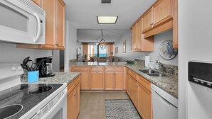 A kitchen with wooden cabinets, granite countertops, a microwave, stove, and dishwasher. - Gulf front! 3rd floor right on the beach! With free beach service (Navarre)