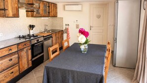 Une cuisine compacte dotée de meubles en bois, d’une cuisinière à gaz, d’un four encastré, d’un réfrigérateur et d’une table à manger avec des chaises.
