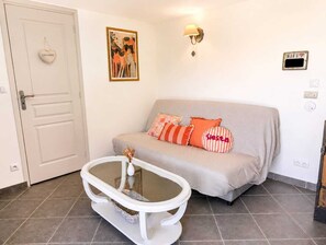 Une pièce avec un canapé beige, une table basse blanche, une porte ornée d’un motif en forme de cœur, un luminaire fixé au mur et un panneau indiquant la présence d’une connexion Wi-Fi.
