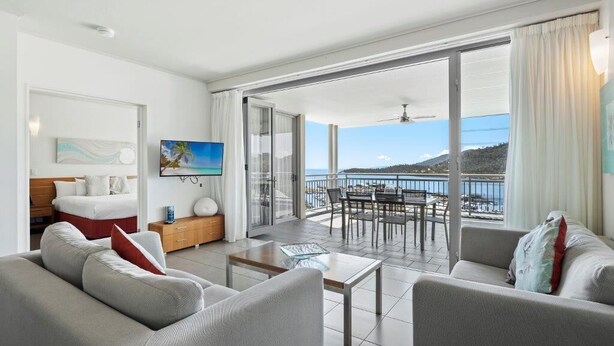 A modern living room with a large sliding glass door leading to a balcony with a view of the sea. - Sea La Vie - Airlie Beach (Airlie Beach)