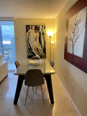 Ein Essbereich mit einem Glastisch, Stühlen, einem großen abstrakten Gemälde und einer Stehlampe.