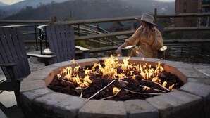 Une personne qui entretient un foyer extérieur, avec une chaîne de montagnes en arrière-plan.