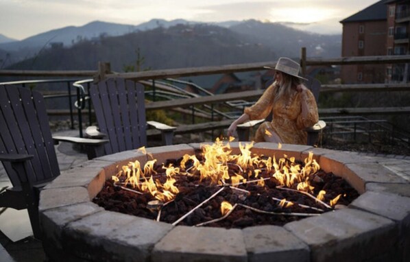 A person tending to a fire pit with a mountainous backdrop.