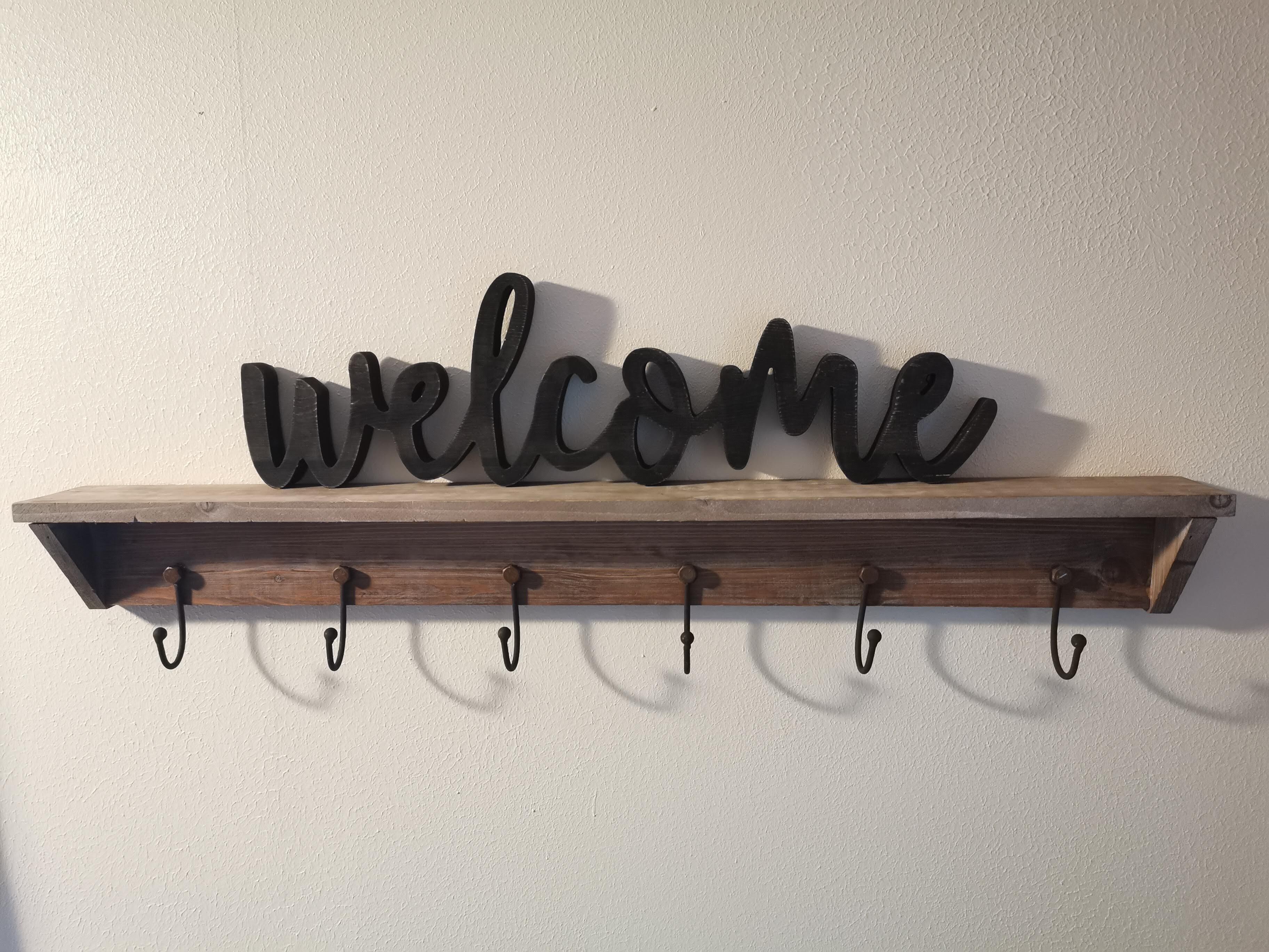 A wooden shelf with a 'welcome' sign and six hooks.