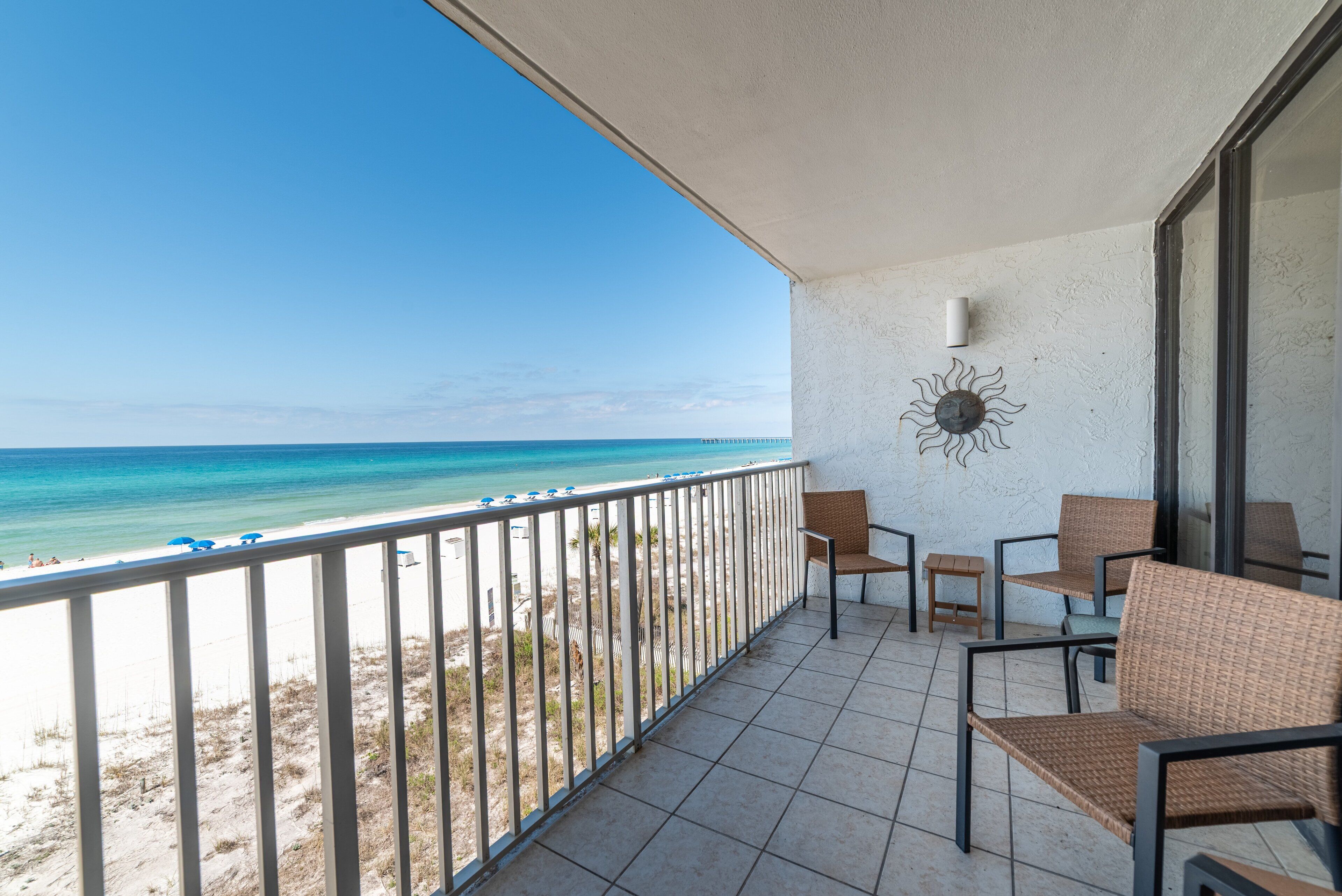 Een balkon met uitzicht op het strand en de oceaan, voorzien van rieten stoelen en een klein tafeltje.