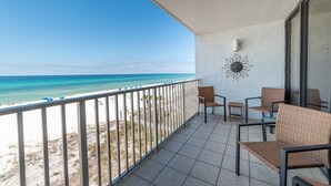 Varanda com vista para a praia e oceano, com cadeiras de vime e uma pequena mesa.
