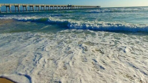 Uma praia com ondas e um cais ao fundo.