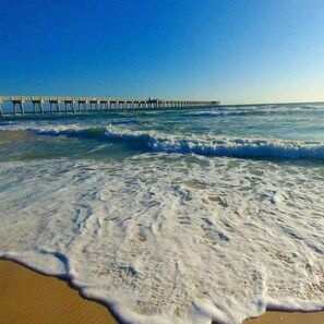 A beach with waves and a pier in the background.