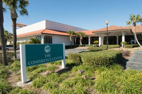 A building with a sign reading "The Conference Center" surrounded by greenery and palm trees.