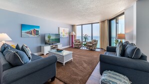 Un salon moderne doté d’une grande fenêtre, d’un téléviseur à écran plat et d’un coin salon confortable avec deux canapés et une table basse.