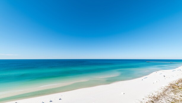 Une vaste plage aux eaux turquoise et limpides, et une longue jetée qui s’avance dans la mer.