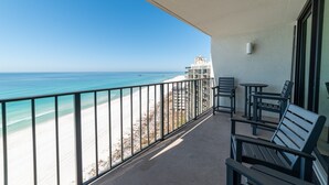 Un balcon avec vue sur la plage et l’océan, comprenant une balustrade, une table et deux chaises.
