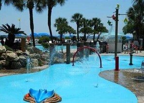 Relax by the central pool surrounded by lush tropical plants and palm trees, featuring a fun water slide.