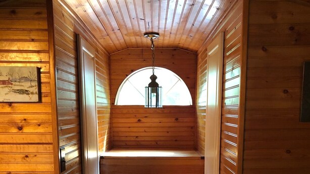 Interior de madera con una escalera que lleva a una ventana con un farol.