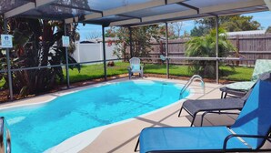 A covered outdoor swimming pool with lounge chairs and a wooden fence in the background. - Private HEATED Pool home in Port Richey / Essentials Provided during your stay  (Port Richey)
