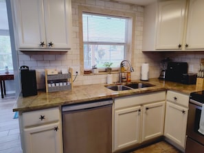 A kitchen with white cabinets, a double sink, a built-in dishwasher, and a window with blinds.