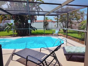 A covered swimming pool area with lounge chairs and a chair with a cushion.