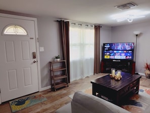 A living room with a television, a door, a small plant, and a wooden shelf.