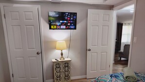 A bedroom with two beds, a TV mounted on the wall, and a bedside table with a lamp. - Private HEATED Pool home in Port Richey / Essentials Provided during your stay  (Port Richey)