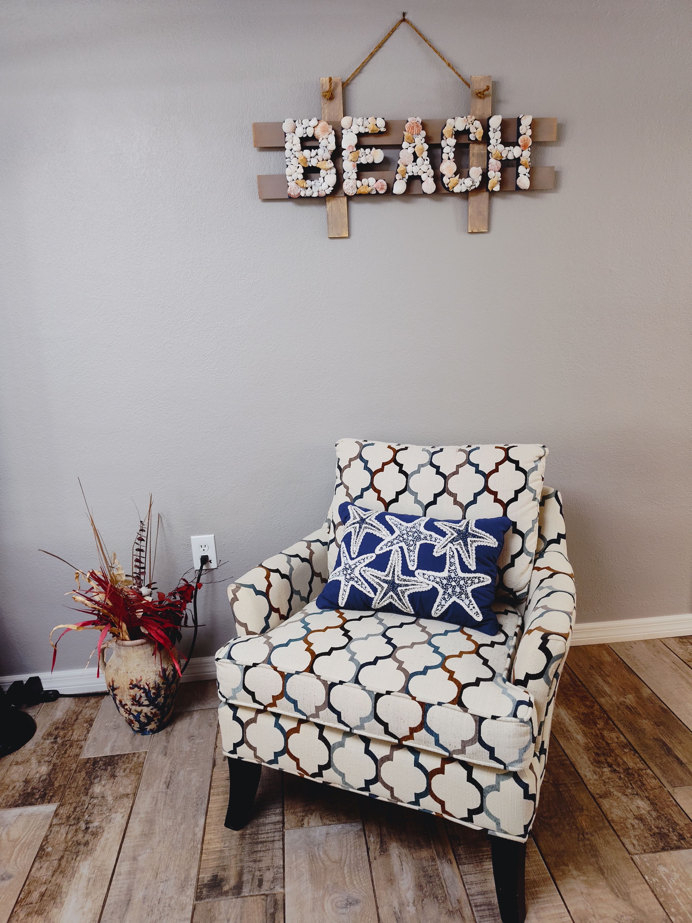 A room with a wooden chair, a wall-mounted sign reading 'BEACH,' and a patterned cushion.