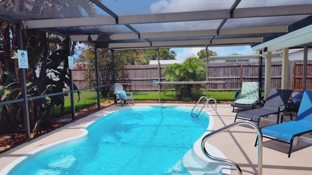 A covered swimming pool with lounge chairs and a wooden fence in the background. - Private HEATED Pool home in Port Richey / Essentials Provided during your stay  (Port Richey)