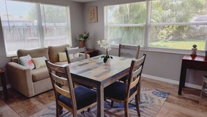 A dining area with a wooden table, chairs, a sofa, and a view of the outdoors through large windows. - Private HEATED Pool home in Port Richey / Essentials Provided during your stay  (Port Richey)