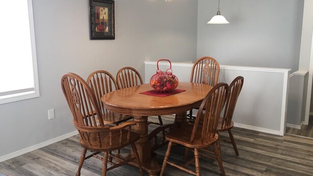 Un comedor con una mesa redonda de madera, seis sillas de madera, una cesta roja y una lámpara de araña.