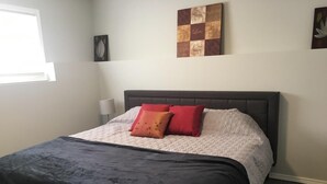 Una cama bien hecha con un cabecero oscuro, dos almohadas rojas y una colcha blanca.